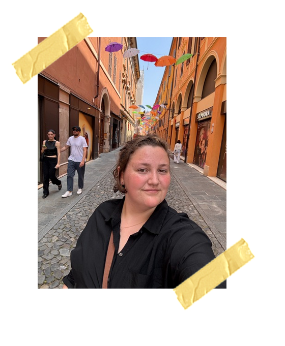 A photo of me on the streets of Siena under an art installation with a bunch of colorful umbrellas.